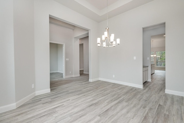 spare room featuring a tray ceiling, light hardwood / wood-style flooring, and a notable chandelier