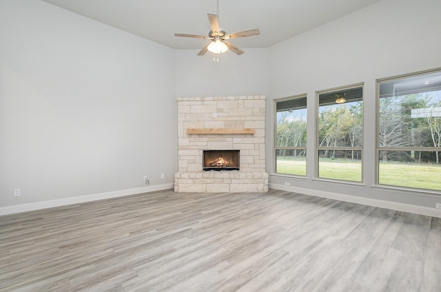 unfurnished living room with ceiling fan, a towering ceiling, a fireplace, and light hardwood / wood-style flooring