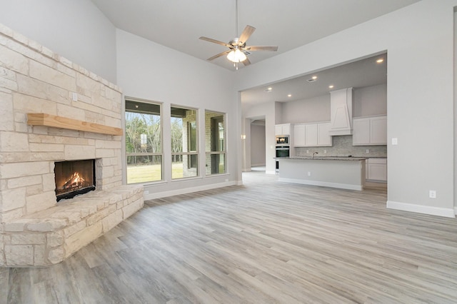 unfurnished living room featuring a stone fireplace, ceiling fan, high vaulted ceiling, and light hardwood / wood-style floors