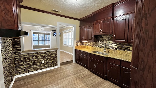 kitchen with light stone countertops, sink, crown molding, light hardwood / wood-style floors, and a textured ceiling