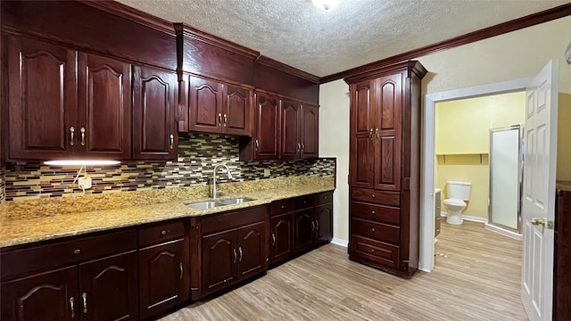 kitchen featuring light stone countertops, light wood-type flooring, backsplash, crown molding, and sink