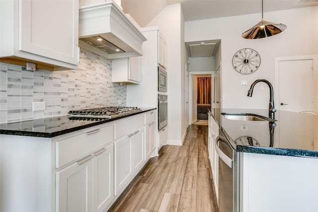 kitchen with decorative backsplash, appliances with stainless steel finishes, premium range hood, sink, and white cabinetry