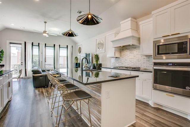 kitchen with a kitchen bar, a kitchen island with sink, lofted ceiling, and appliances with stainless steel finishes