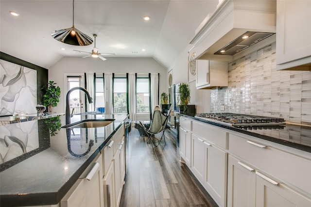 kitchen with stainless steel gas stovetop, lofted ceiling, wall chimney range hood, sink, and white cabinetry