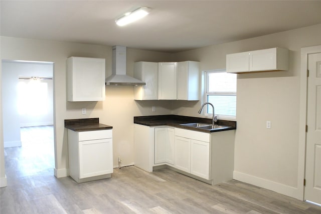 kitchen with white cabinets, light wood-type flooring, sink, and wall chimney range hood