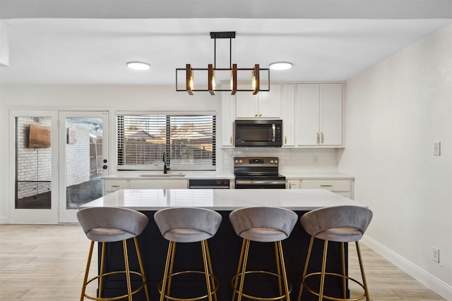 kitchen with pendant lighting, backsplash, stainless steel range with electric cooktop, white cabinets, and sink