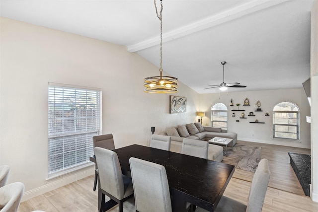 dining space featuring ceiling fan with notable chandelier, vaulted ceiling with beams, light wood-type flooring, and a healthy amount of sunlight