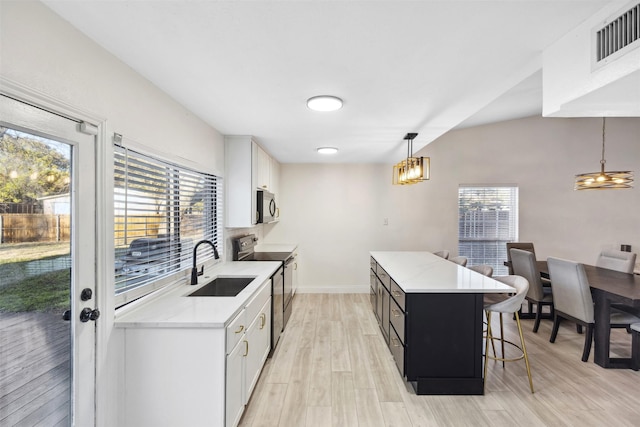 kitchen with sink, electric range, light hardwood / wood-style flooring, white cabinets, and hanging light fixtures