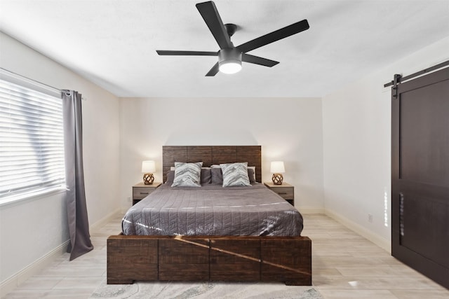 bedroom featuring ceiling fan, a barn door, and light hardwood / wood-style flooring