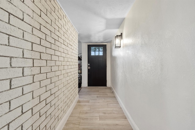 doorway with light hardwood / wood-style flooring, brick wall, and a textured ceiling