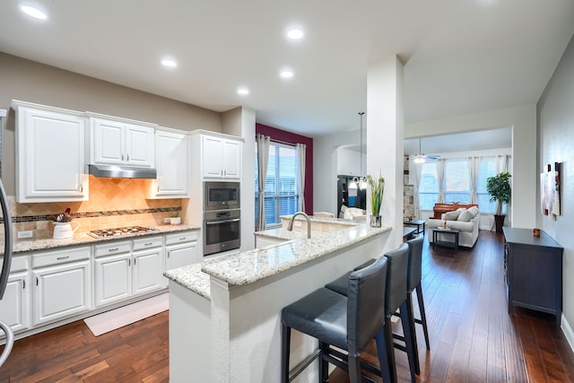 kitchen featuring a breakfast bar, appliances with stainless steel finishes, white cabinetry, and light stone counters