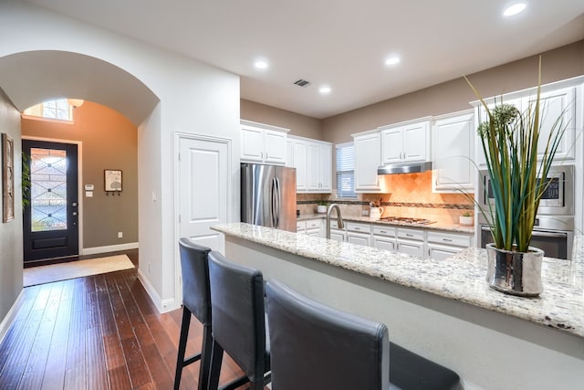 kitchen with light stone counters, dark hardwood / wood-style flooring, backsplash, white cabinets, and appliances with stainless steel finishes