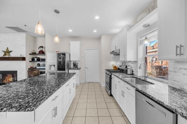 kitchen with dark stone counters, white cabinets, sink, appliances with stainless steel finishes, and a large fireplace