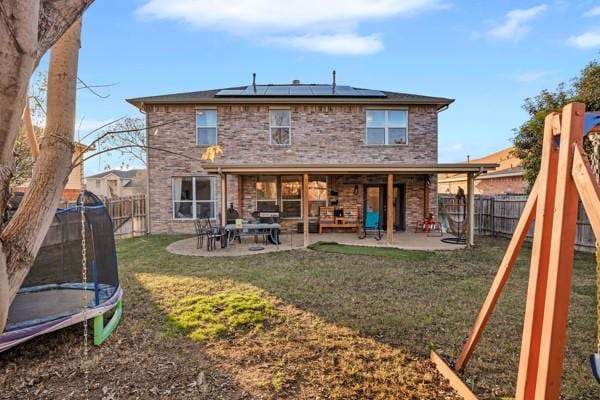 back of property with a playground, a trampoline, a patio, and a lawn