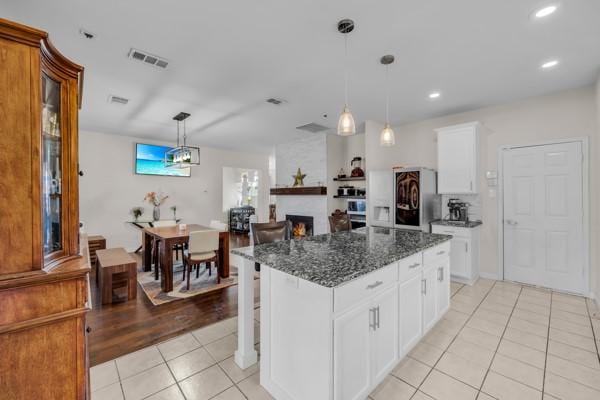 kitchen with white cabinetry, a large fireplace, a center island, dark stone counters, and light tile patterned flooring