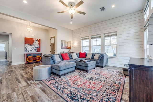 living room with ceiling fan with notable chandelier, wood-type flooring, and wooden walls