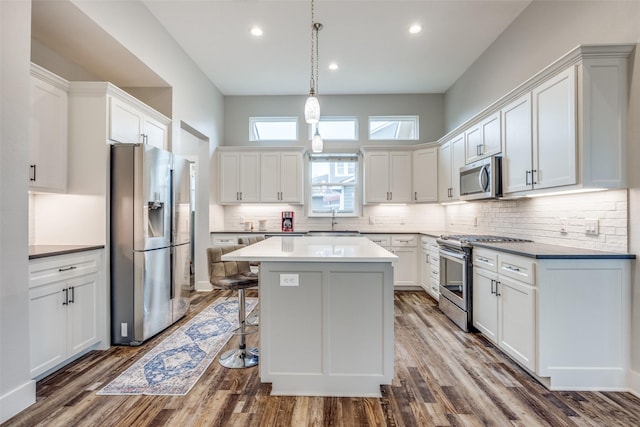 kitchen featuring tasteful backsplash, wood-type flooring, appliances with stainless steel finishes, pendant lighting, and white cabinets