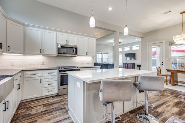 kitchen featuring white cabinetry, hanging light fixtures, dark hardwood / wood-style flooring, and appliances with stainless steel finishes