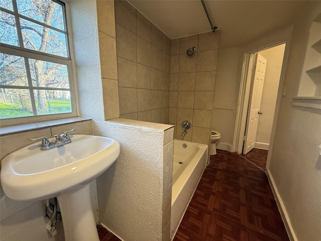 bathroom with tiled shower / bath combo, parquet flooring, and toilet