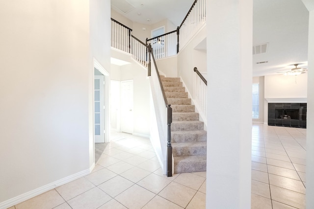 stairway with tile patterned floors, a tile fireplace, ceiling fan, and a towering ceiling