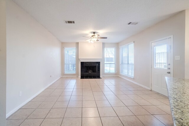 unfurnished living room featuring light tile patterned floors, a textured ceiling, ceiling fan, and a tiled fireplace