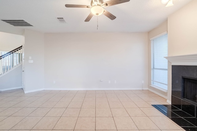 unfurnished living room featuring ceiling fan, light tile patterned floors, a textured ceiling, and a tiled fireplace