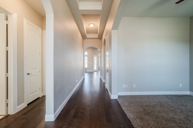 hall with a raised ceiling and dark wood-type flooring