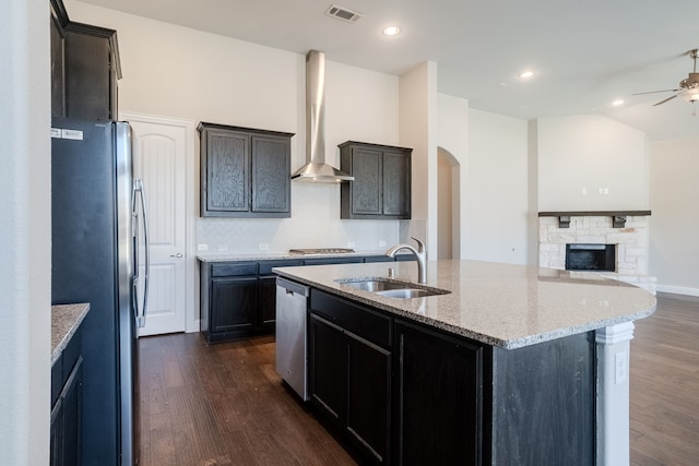 kitchen with backsplash, wall chimney range hood, sink, an island with sink, and stainless steel appliances