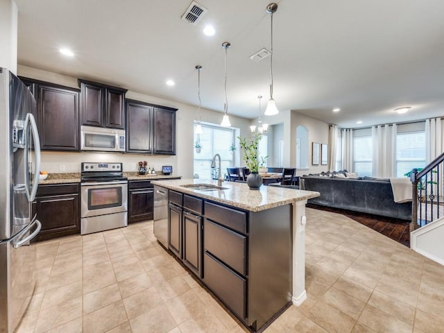 kitchen featuring appliances with stainless steel finishes, decorative light fixtures, sink, a center island with sink, and dark brown cabinets