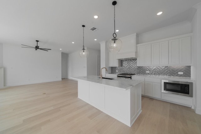 kitchen featuring built in microwave, white cabinetry, hanging light fixtures, a kitchen island with sink, and custom range hood