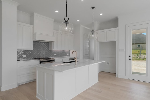 kitchen with sink, white cabinetry, stainless steel gas range oven, a center island with sink, and decorative light fixtures