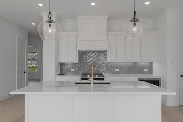 kitchen featuring light stone countertops, a kitchen island with sink, and pendant lighting