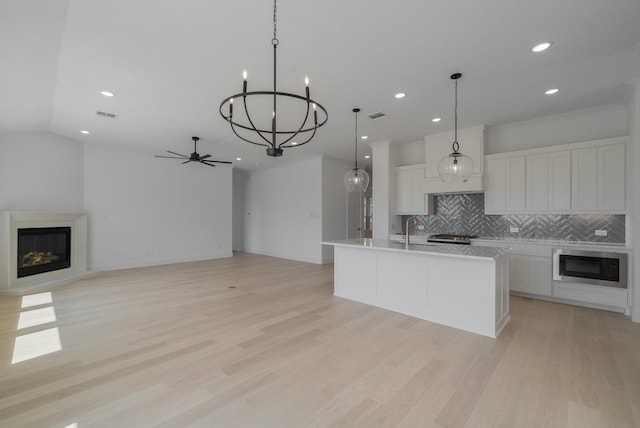 kitchen featuring built in microwave, a center island with sink, light hardwood / wood-style flooring, hanging light fixtures, and white cabinets