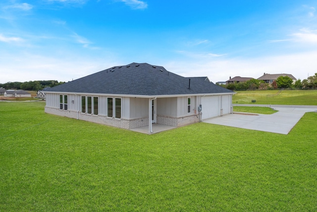 rear view of property featuring a garage, a lawn, and a patio area