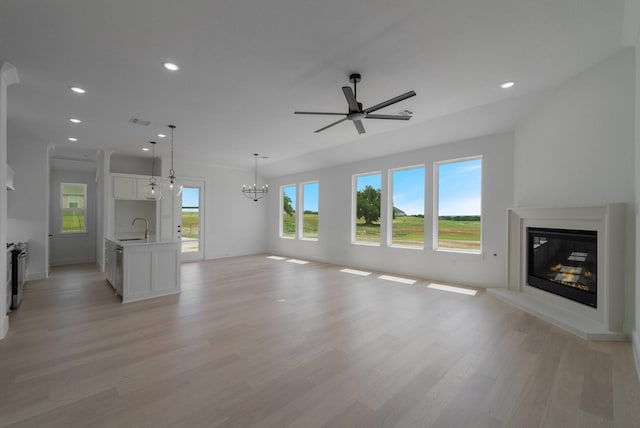 unfurnished living room featuring ceiling fan with notable chandelier, sink, and light hardwood / wood-style floors