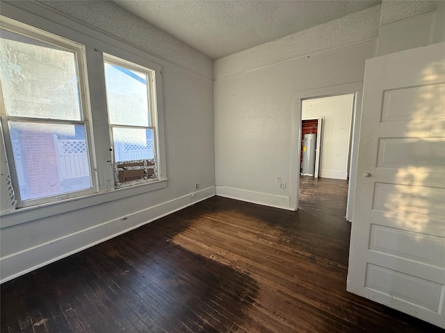 spare room with water heater, dark hardwood / wood-style flooring, and a textured ceiling