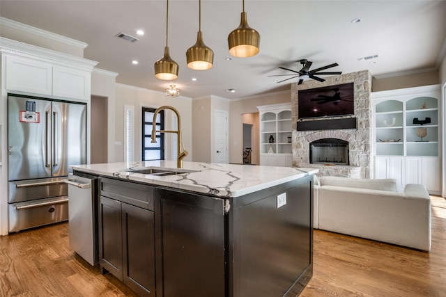 kitchen featuring pendant lighting, a kitchen island with sink, a fireplace, appliances with stainless steel finishes, and light stone counters