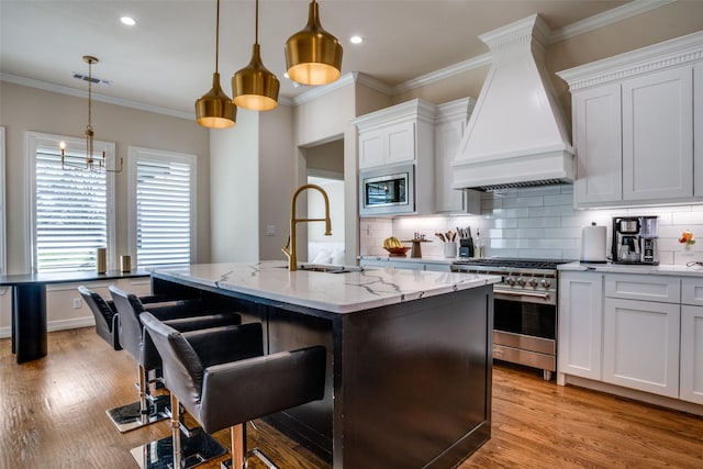 kitchen with appliances with stainless steel finishes, custom exhaust hood, sink, a center island with sink, and white cabinetry