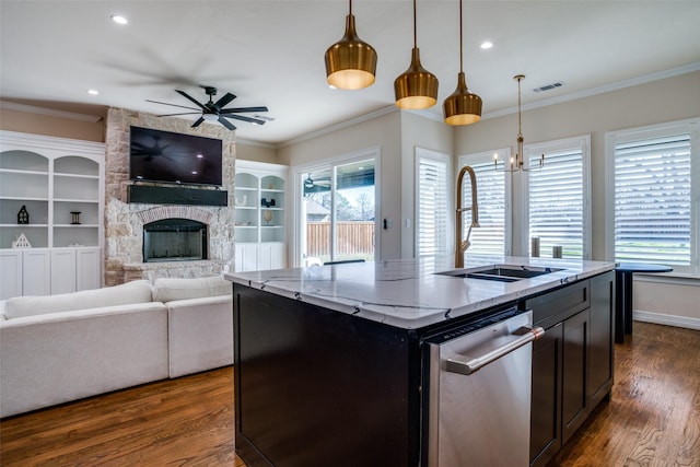 kitchen with sink, light stone counters, dark hardwood / wood-style floors, an island with sink, and pendant lighting