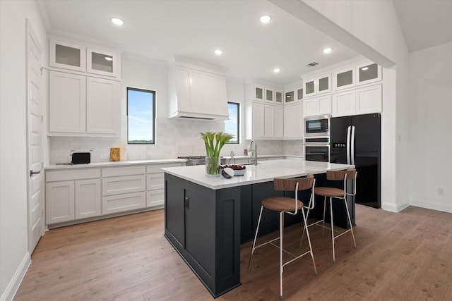 kitchen featuring white cabinetry, built in microwave, black fridge, and a center island with sink