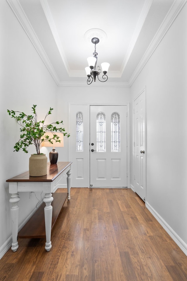 entryway with a tray ceiling, crown molding, dark hardwood / wood-style floors, and an inviting chandelier