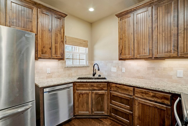 kitchen with tasteful backsplash, sink, light stone countertops, and appliances with stainless steel finishes