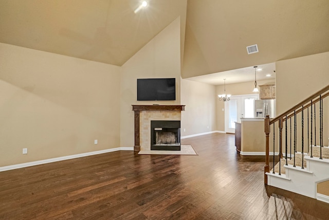 unfurnished living room featuring a tiled fireplace, a notable chandelier, dark wood-type flooring, and high vaulted ceiling