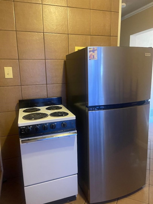 kitchen featuring light tile patterned flooring, stainless steel refrigerator, tile walls, ornamental molding, and white range with electric cooktop