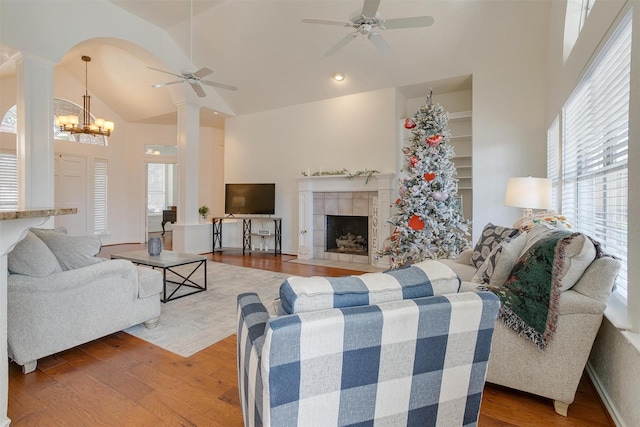 living room featuring dark hardwood / wood-style flooring, high vaulted ceiling, decorative columns, a fireplace, and ceiling fan with notable chandelier