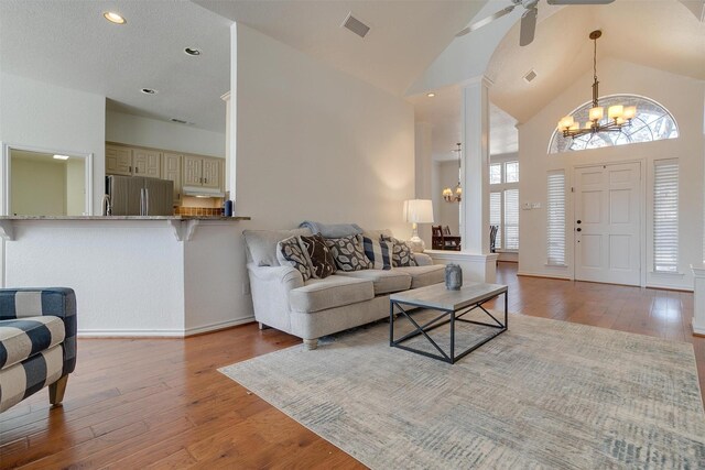 living room with ceiling fan with notable chandelier, light wood-type flooring, and high vaulted ceiling