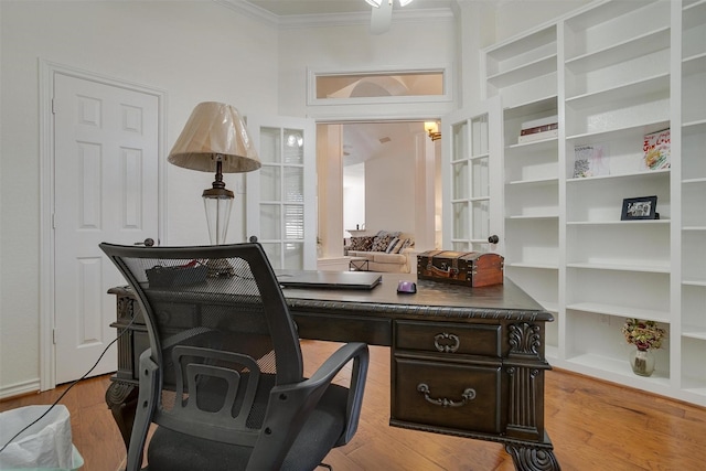 home office featuring crown molding, built in shelves, and light wood-type flooring