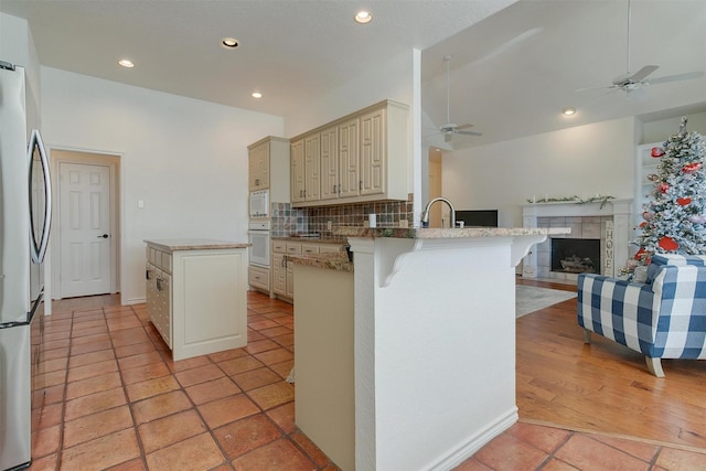 kitchen featuring backsplash, kitchen peninsula, white appliances, cream cabinetry, and a breakfast bar area