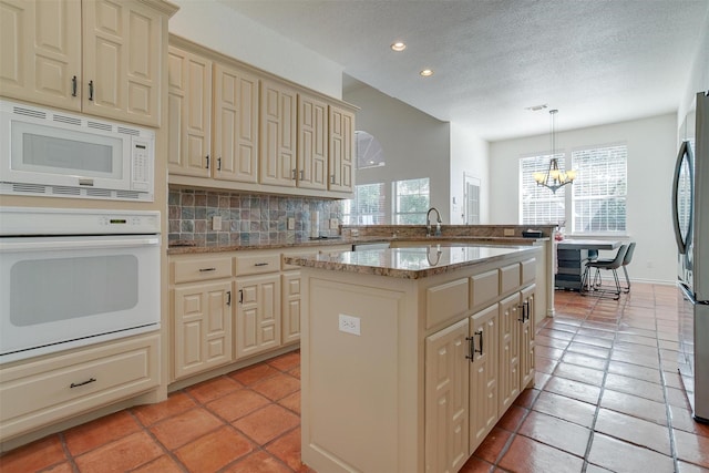 kitchen with decorative backsplash, white appliances, pendant lighting, cream cabinetry, and a kitchen island