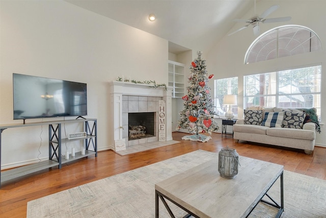 living room with a tile fireplace, hardwood / wood-style flooring, high vaulted ceiling, and ceiling fan